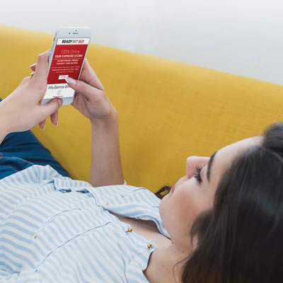 Young woman laying back on couch as she scrolls through her email inbox